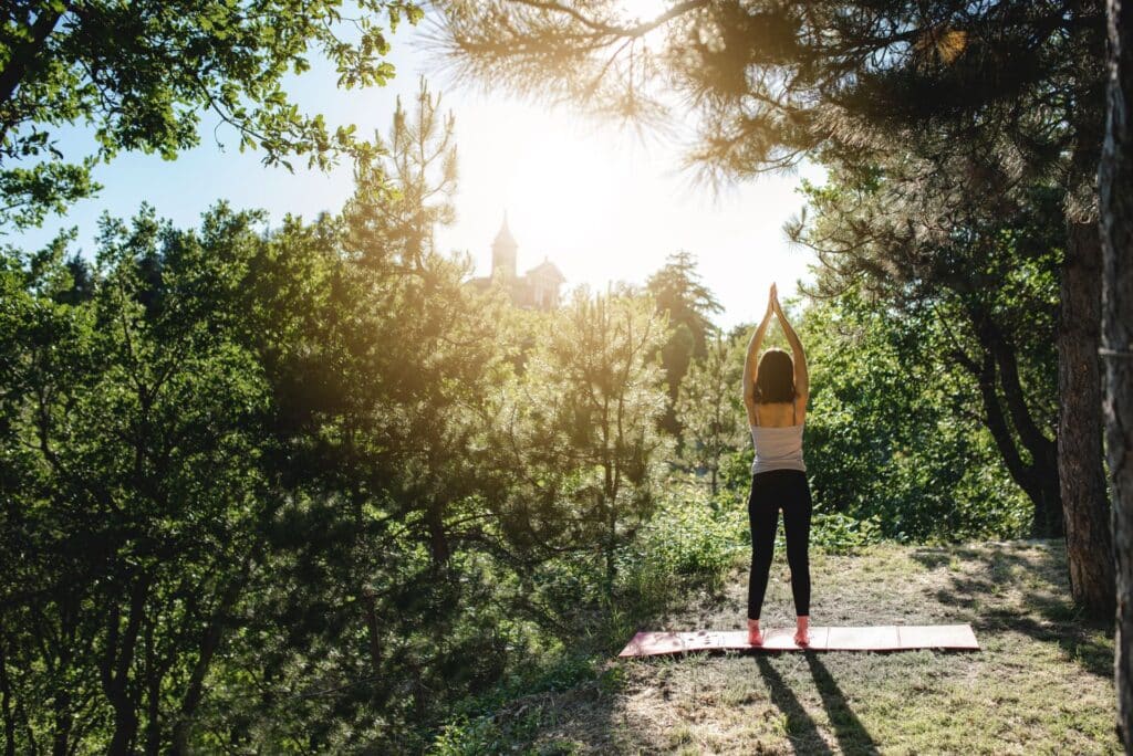 Frau bei einer Yoga-Pose im Wald mit Sonnenlicht, ideal ergänzt durch einen nahegelegenen Gartenpavillon für Schutz und Komfort.