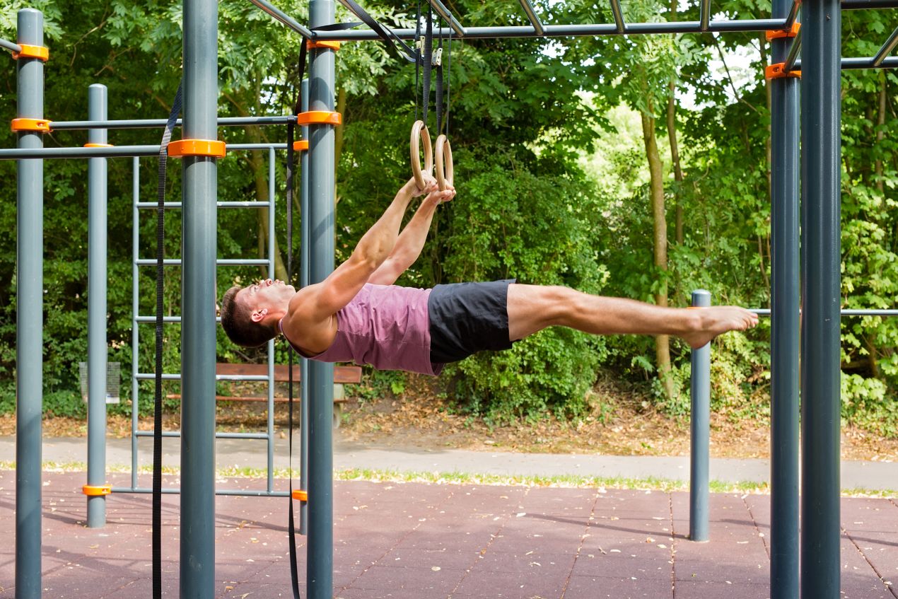 Sportler haelt statische Position an Ringen bei Calisthenics-Workout im Outdoor-Park